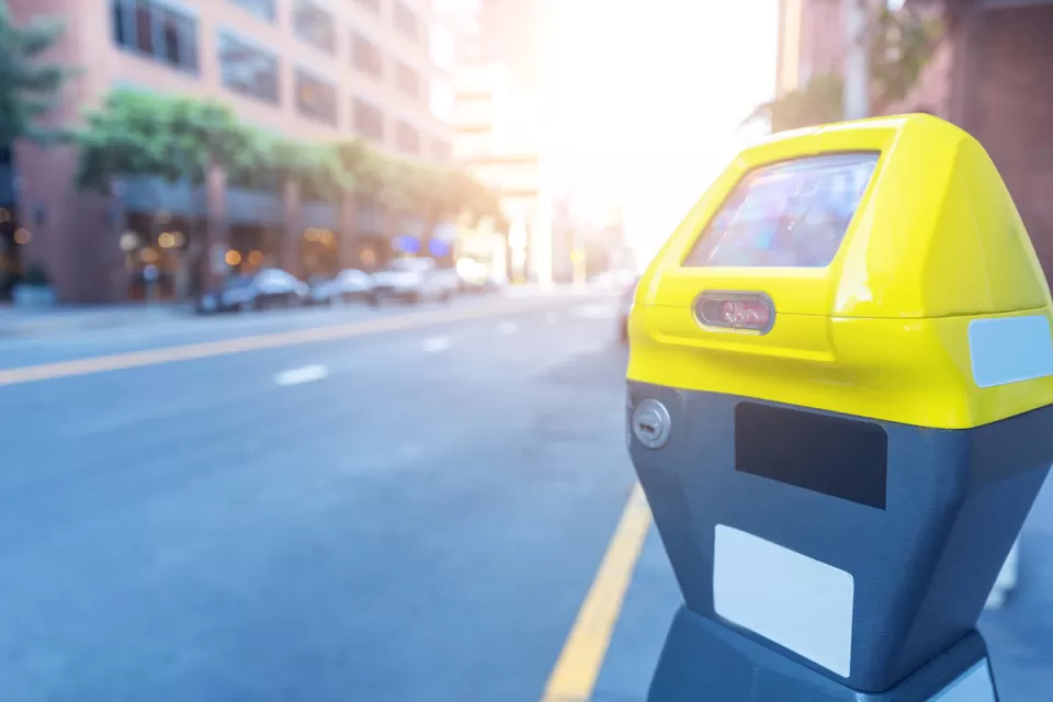 Close-up of yellow and grey smart parking meter with blurred city street in background.